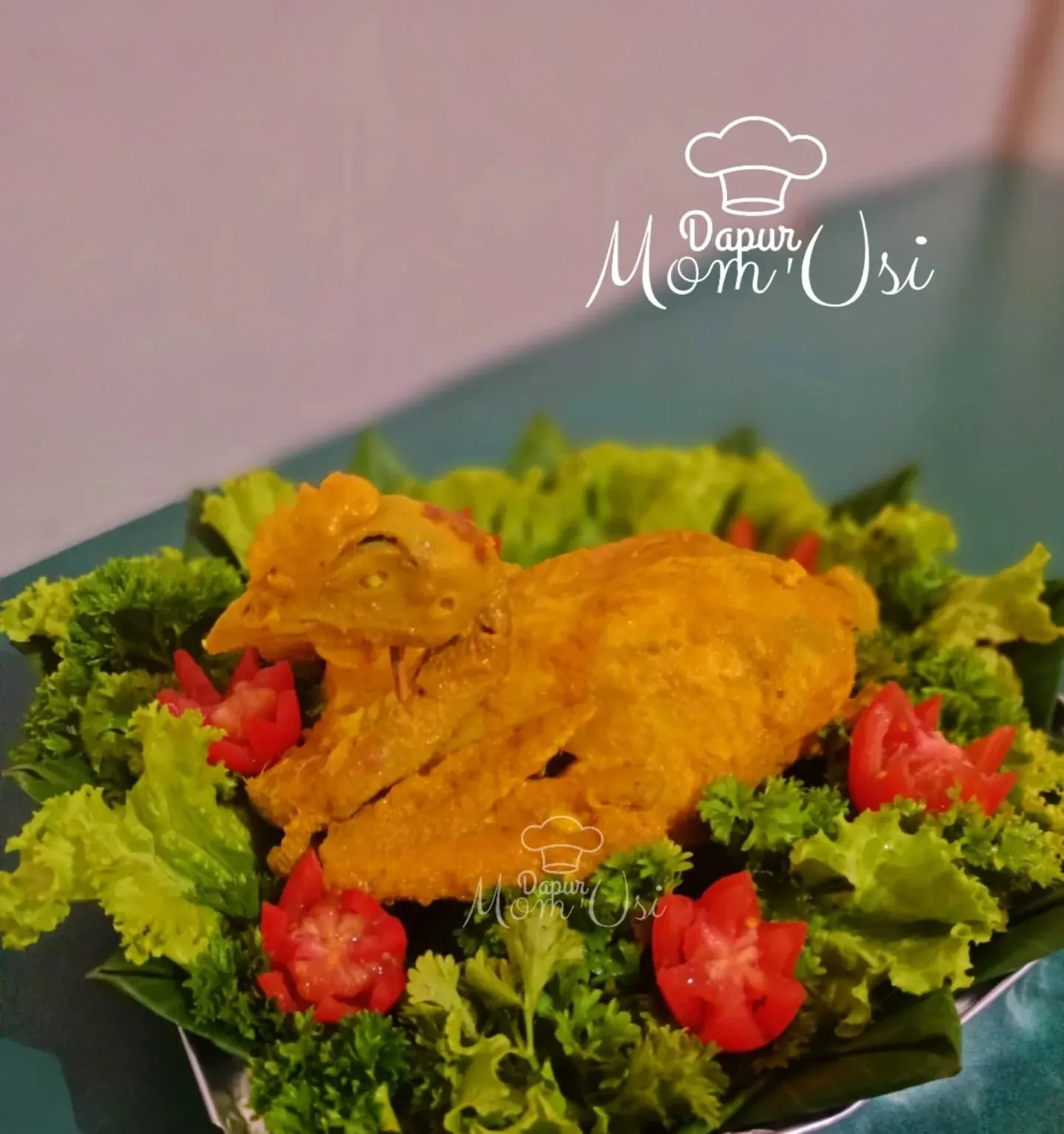 Ayam ingkung utuh berbumbu kuning di atas alas selada dengan hiasan tomat